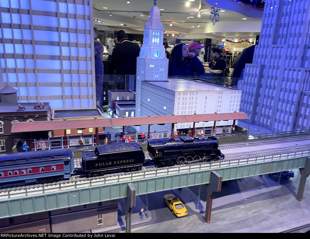 The model polar express train runs on the elevated structure with the model tall buildings in the background.